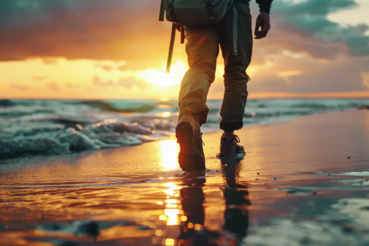 A person strolling along the shoreline as the sun sets behind them